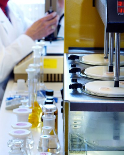 Chemical lab equipment and flasks in the foreground, a lab worker in the background.