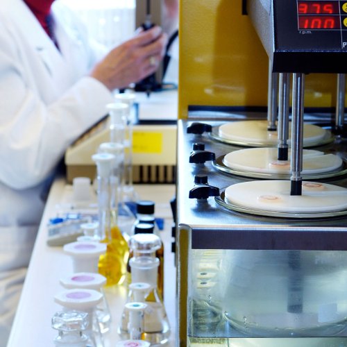 Chemical lab equipment and flasks in the foreground, a lab worker in the background.