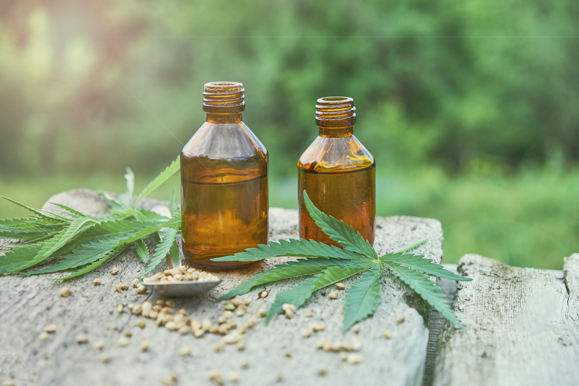 Two brown bottles on a rock surrounded by 2 cannabis leaves and cannabis seeds.